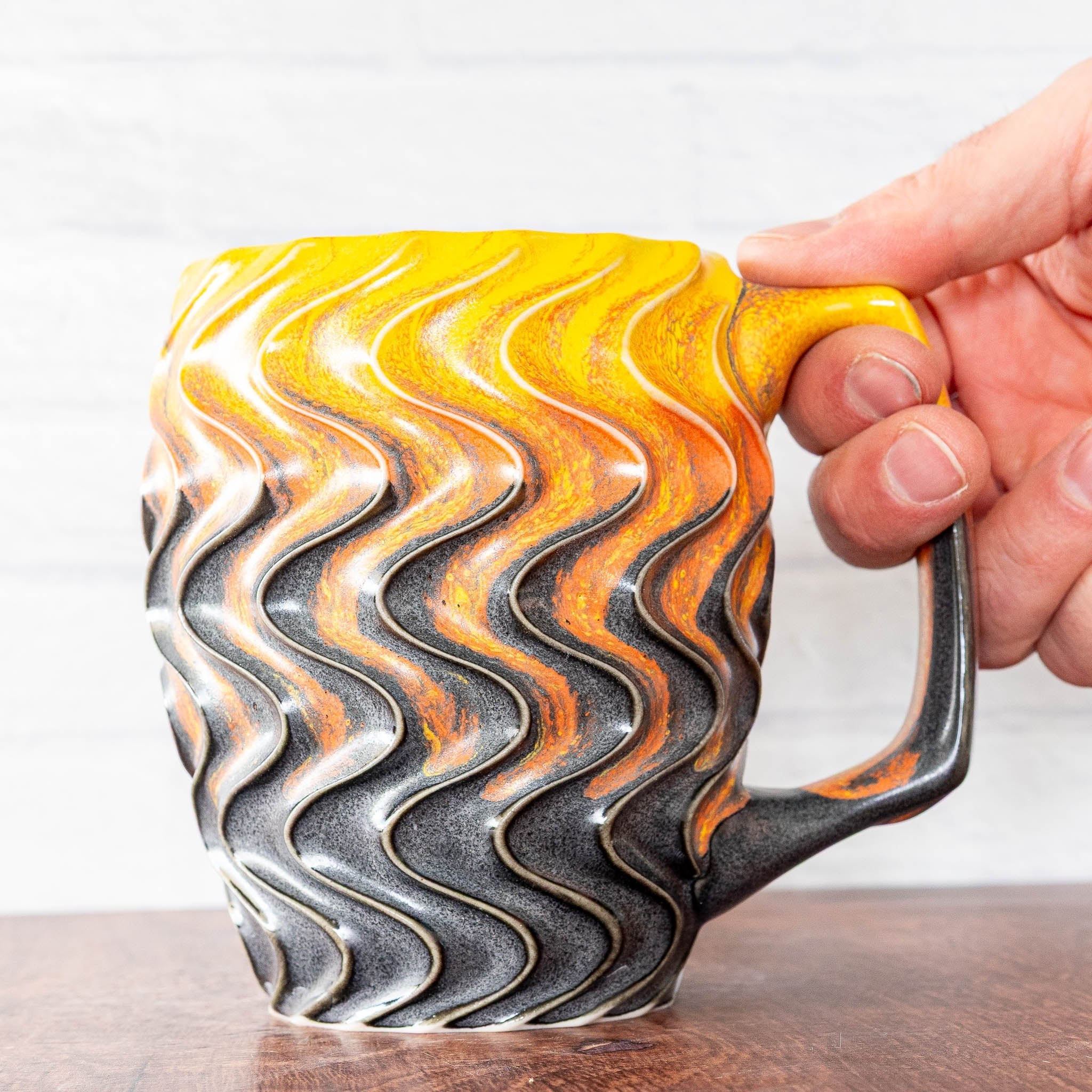Hammerly Ceramics handmade slip-cast mug in cascading orange and yellow over matte black, deep wavy textured porcelain with angular handle