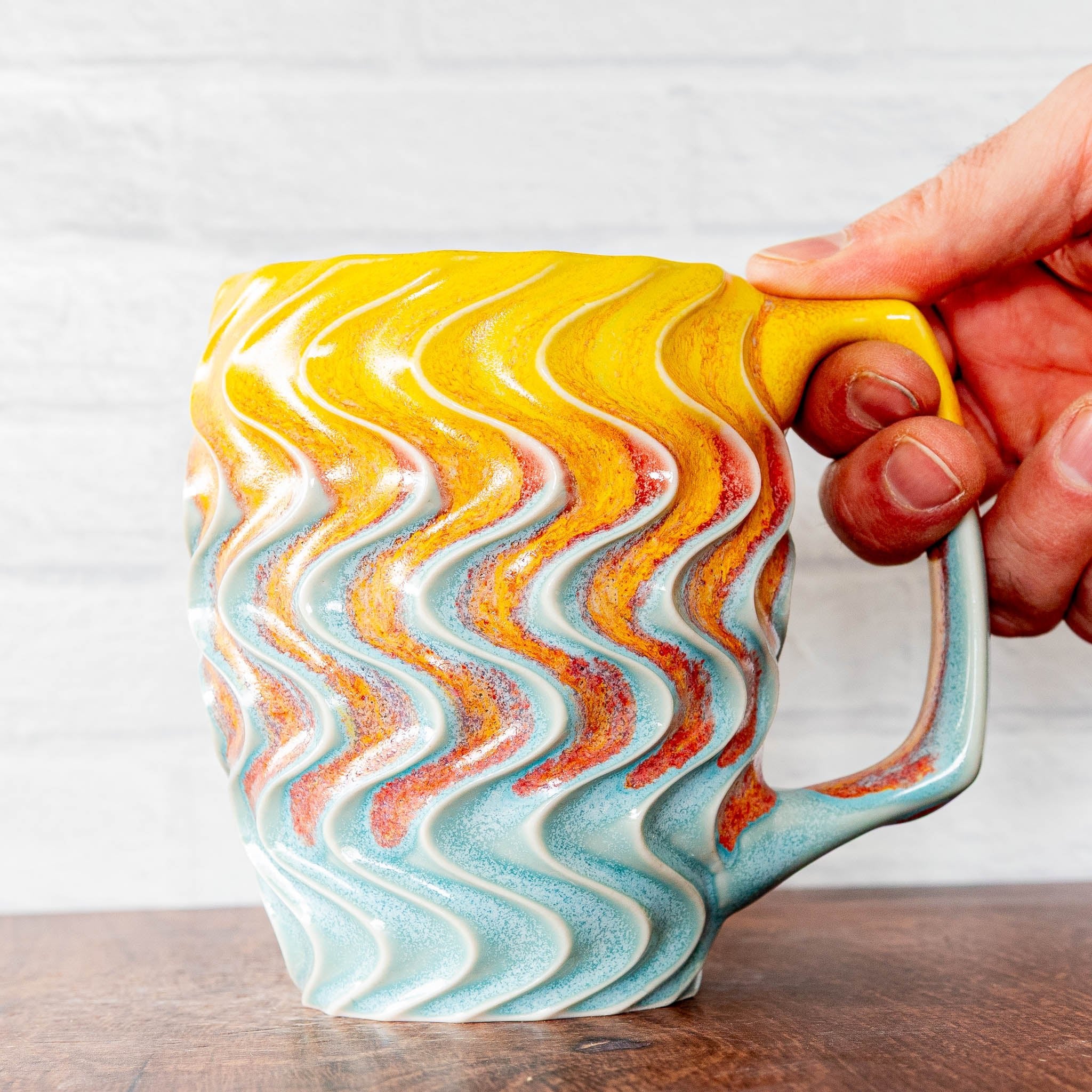 Hammerly Ceramics handmade slip-cast mug in yellow and sky blue with flowing orange blush, deep wavy textured porcelain with angular handle