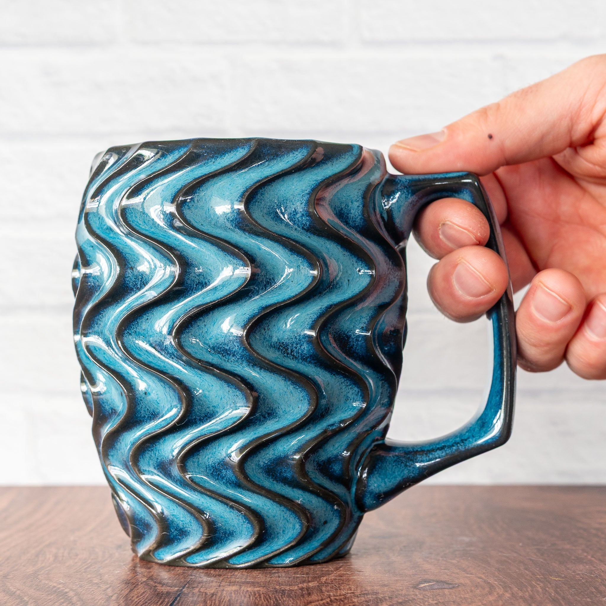 Hammerly Ceramics handmade slip-cast mug in ocean blue glaze with dark charcoal edges, deep wavy textured porcelain with angular handle