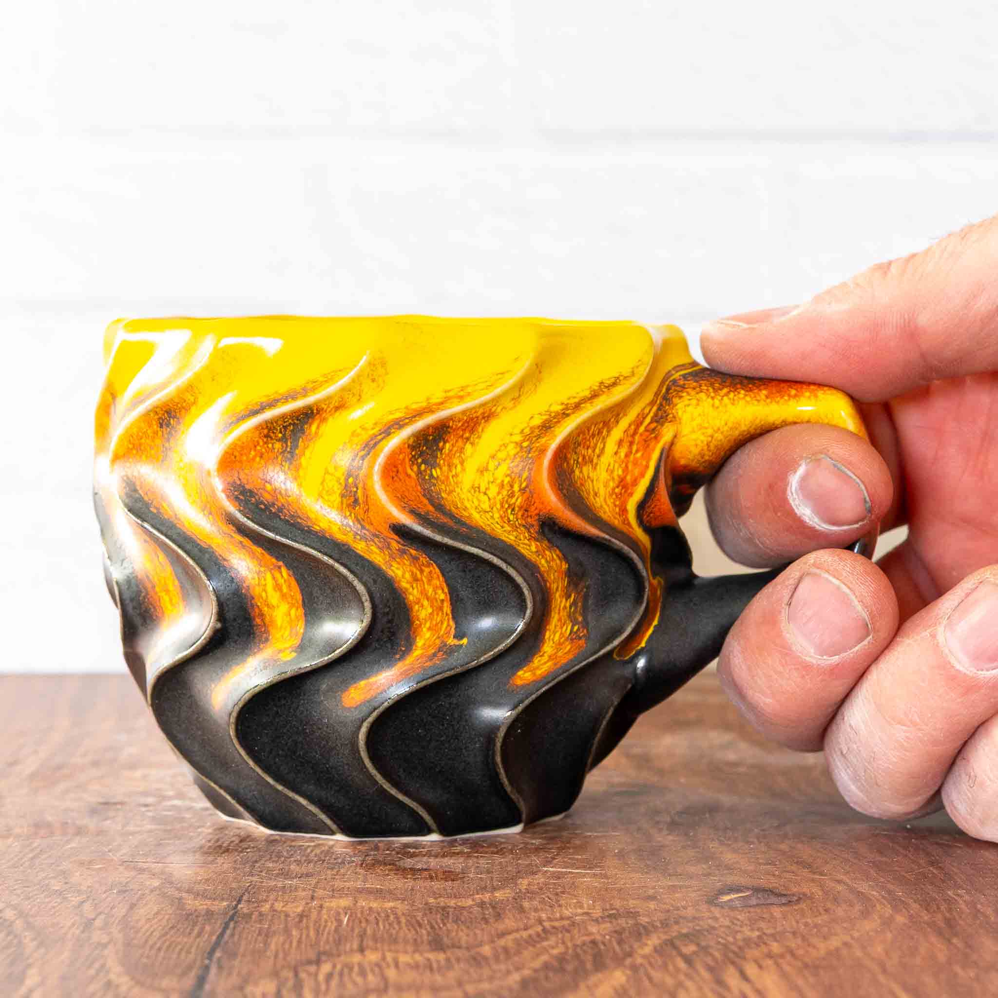 Hammerly Ceramics handmade slip-cast mug in cascading orange and yellow over matte black, deep wavy textured porcelain with angular handle