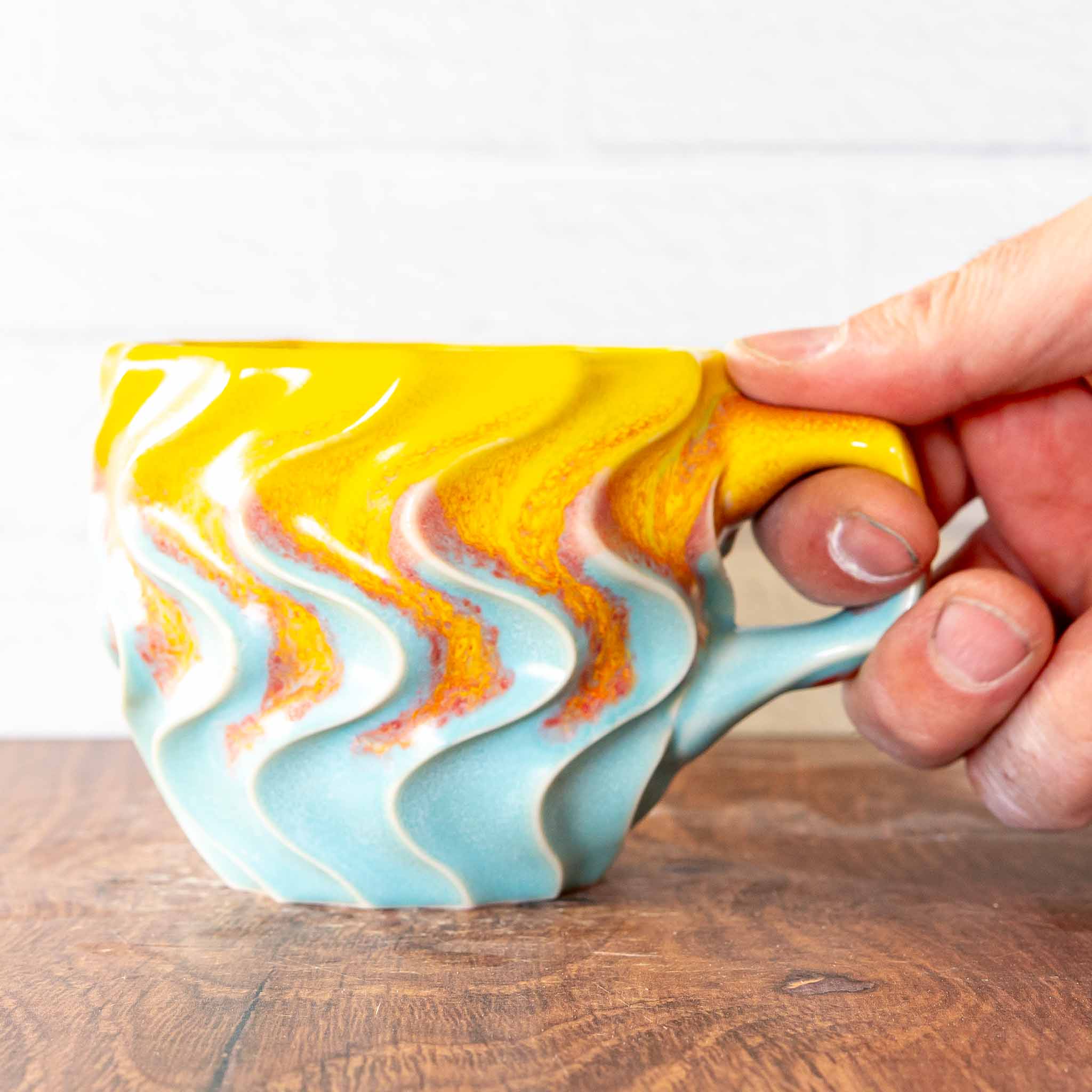 Hammerly Ceramics handmade slip-cast mug in yellow and sky blue with flowing orange blush, deep wavy textured porcelain with angular handle